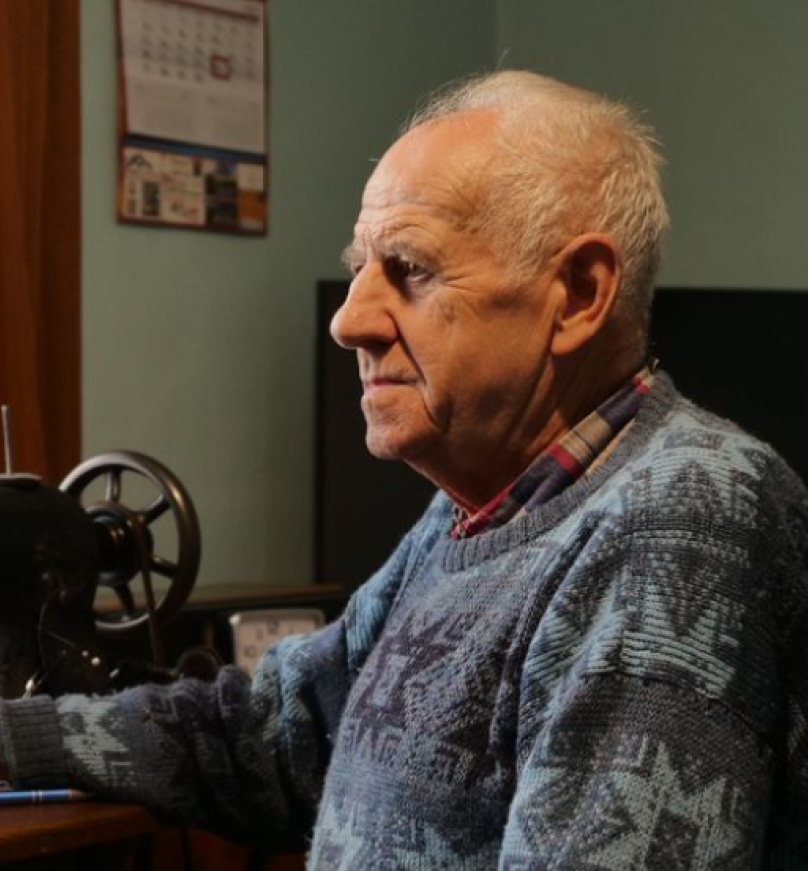 Portret mężczyzny siedzącego przed maszyną do szycia. Link do nagrania fragmentu jego relacji historii mówionej