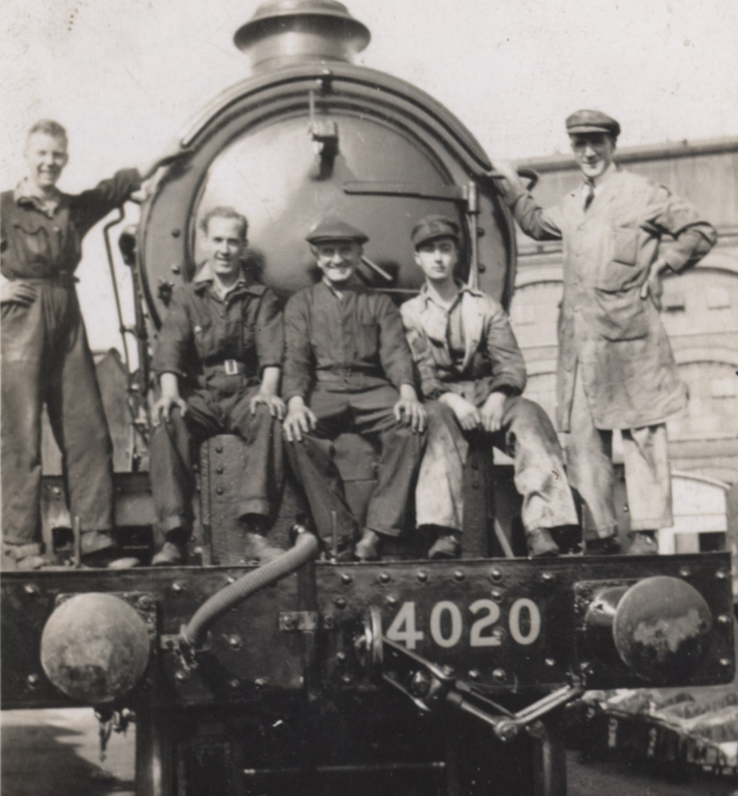 Pięciu mężczyzn w roboczych strojach pozujących do zdjęcia przed parowozem. Link do wyników wyszukiwania hasła kolejarze